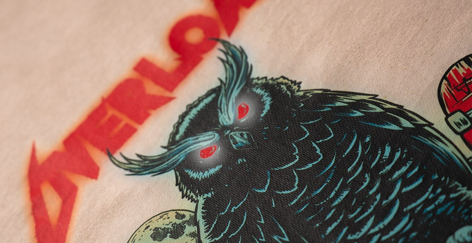 Close-up of a graphic t-shirt featuring a stylized black and teal owl with glowing red eyes holding a moon, beneath a red 'OVERLOAD' text graphic.